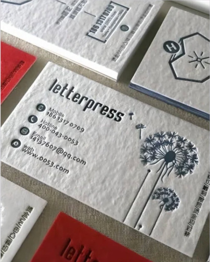 Close-up of debossed letterpress business cards with a dandelion illustration on thick cotton paper.