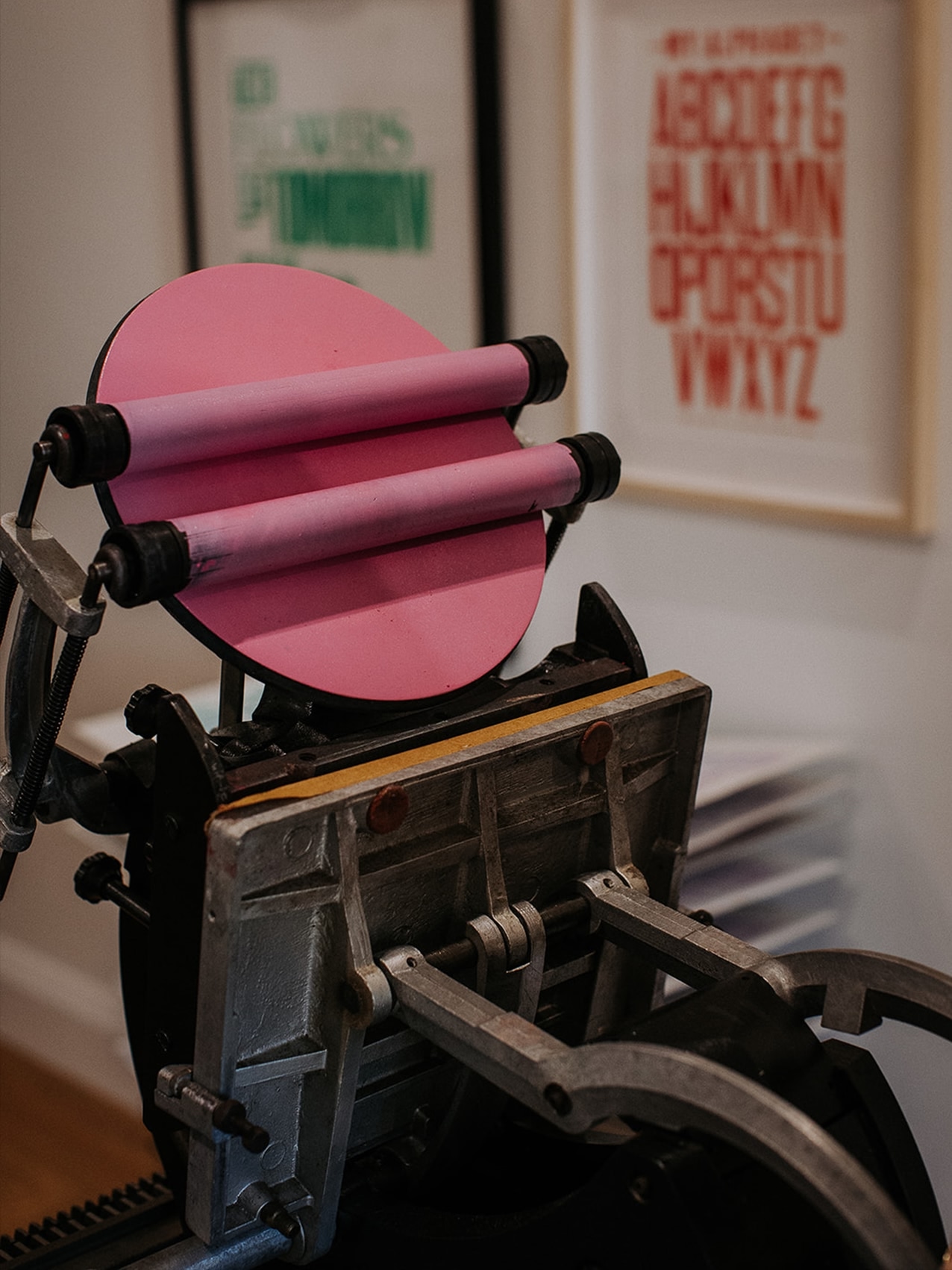 A craftsperson operating a vintage letterpress machine, feeding orange card stock through the press.