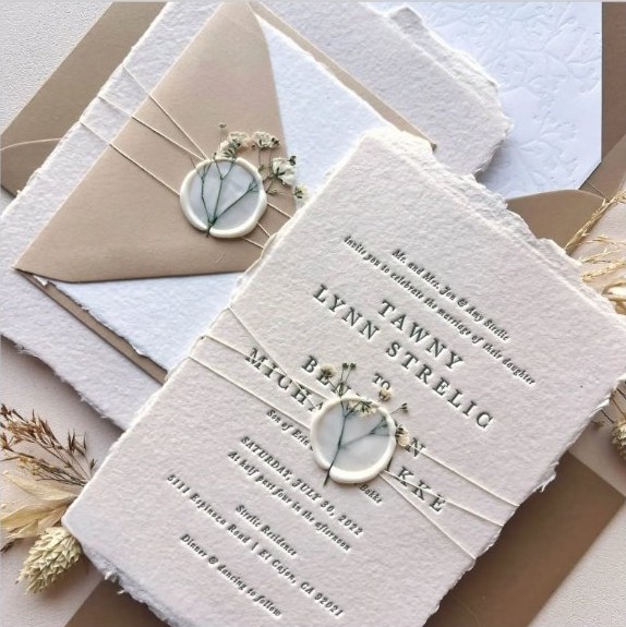 Wedding invitation with wax seal and twine detail on handmade deckle-edge paper.