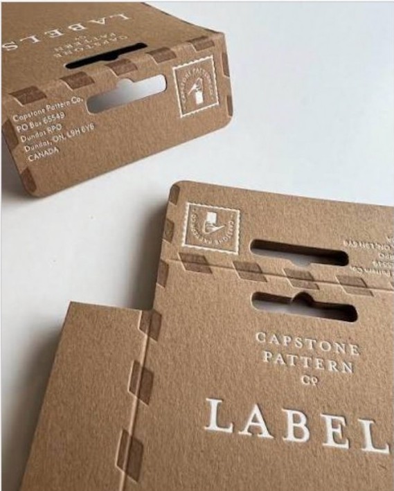 Kraft paper packaging and labels with debossed lettering, stacked on a table.
