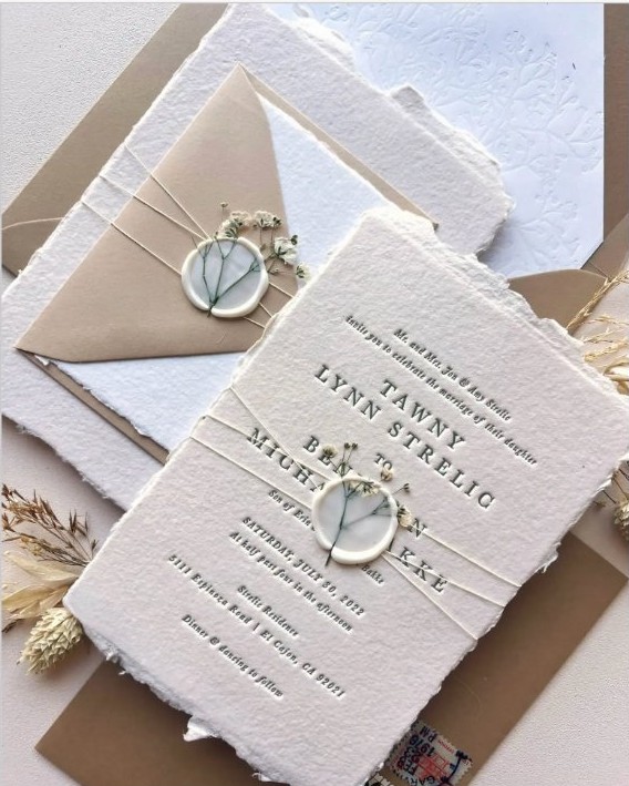 Wedding invitation suite with wax seal, twine, and dried florals on deckle-edge paper.